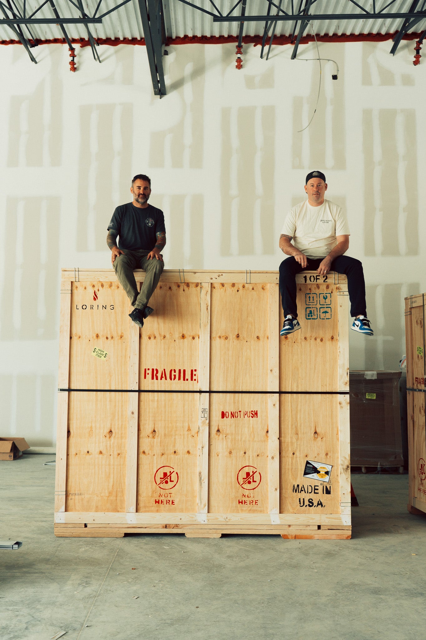 Two men sitting on large wooden crates in a warehouse.